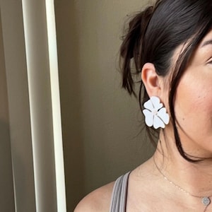 May include: White flower-shaped earrings. The earrings are large and have a delicate, feminine design.