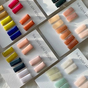 May include: Assortment of colorful rectangular ceramic earrings. The earrings are displayed on white cards with the text "The Olive Leaf Designs".