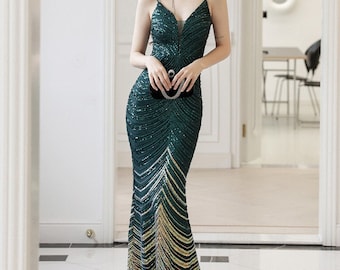 May include: A formal, floor-length emerald green gown with a V-neckline and spaghetti straps. The dress is embellished with sequins and features a mermaid silhouette. The lower portion transitions to a gold and silver chevron pattern. A black clutch is held.