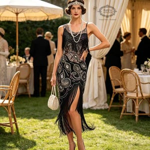 May include: A black sleeveless dress featuring intricate silver embroidery, a high side slit, and long black fringe detailing. The outfit includes a multi-strand pearl necklace, a matching pearl-embellished handbag, and a decorative silver headpiece.