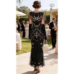 May include: A black beaded evening gown with a sheer overlay and a mermaid silhouette. The dress is adorned with silver and pearl embellishments. The person is wearing long black gloves and carrying a pearl-handled purse. The setting is an outdoor formal event.