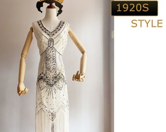 May include: A white beaded flapper dress with fringe detailing. The dress has a geometric pattern and a V-neckline. The dress is on a mannequin with a black hat. The text "1920s STYLE" is in the background.
