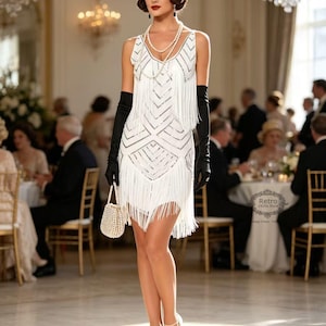 May include: A white sleeveless dress featuring silver geometric sequin patterns and long fringe detailing. The outfit includes a pearl headband, layered pearl necklaces, long black opera gloves, a small beaded handbag, and light-colored heels.
