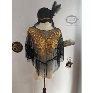 May include: Black sequined shawl with gold butterfly design and fringe trim. The shawl is on a mannequin wearing a black hat with a feather. The text "Retro 1920s Style" is on a white tag. The text "Vintage Dress Headband" is on a white tag. The text "Roaring Twenties" is on a black tag.