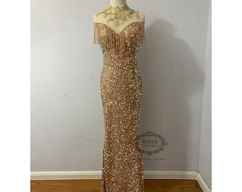 Könnte beinhalten: Ein goldenes Paillettenkleid mit hohem Kragen und Fransen. Das Kleid hat eine figurbetonte Silhouette und einen langen, fließenden Rock.