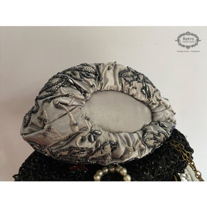 Pu&ograve; includere: Una pochette in satin argento con un motivo floreale perlato. La pochette &egrave; chiusa e ha una forma rotonda.