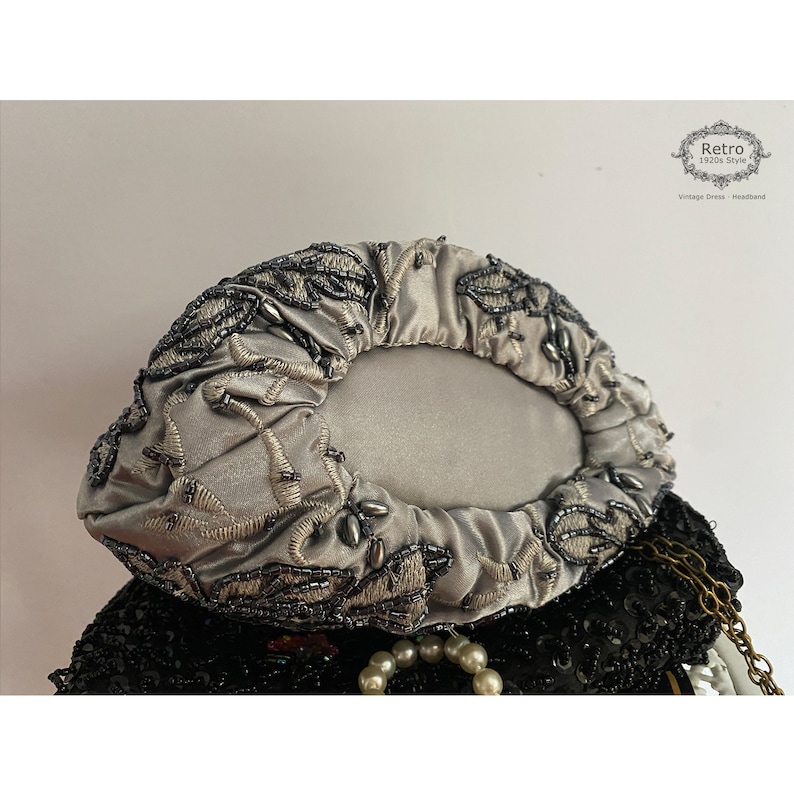 Pu&ograve; includere: Una pochette in satin argento con un motivo floreale perlato. La pochette &egrave; chiusa e ha una forma rotonda.