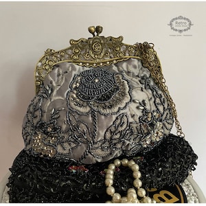 Pu&ograve; includere: Una borsa da sera in satin grigio con un design floreale e decorazioni di perline. La borsa ha una chiusura in ottone e una tracolla a catena.