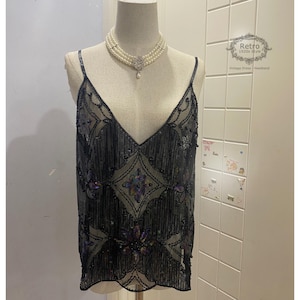 Può includere: Un top nero con paillettes con scollo a V e un motivo geometrico. Il top è realizzato in tessuto trasparente e ha un bordo di perline.