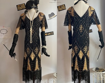 Peut inclure: Une robe de flapper noire et dorée avec des franges et des embellissements perlés. La robe a un décolleté en V et des manches courtes. La robe est sur un mannequin avec un bandeau noir et une plume.