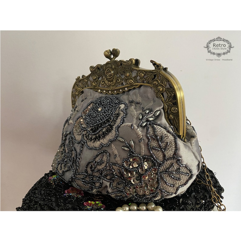 Pu&ograve; includere: Una pochette in satin grigio con un motivo floreale e decorazioni di perline. La pochette ha una chiusura in ottone e una tracolla a catena.