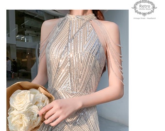 Könnte beinhalten: Ein silbernes Pailletten-Halterkleid mit geometrischem Muster und einem Kettendetail an den Trägern. Das Kleid hat eine figurbetonte Silhouette und einen hohen Ausschnitt.  "Retro 1920s Style" und "Vintage Dress - Headband" stehen in der oberen rechten Ecke des Bildes.