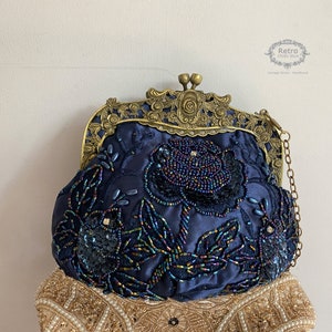 Pu&ograve; includere: Una borsa da sera in satin blu navy con una cornice in metallo dorato e una tracolla a catena. La borsa &egrave; decorata con paillettes e perline iridescenti in un motivo floreale.