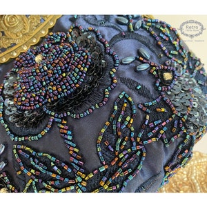 Pu&ograve; includere: Primo piano di un tessuto blu scuro con paillettes e perline iridescenti che formano un motivo floreale. Le paillettes e le perline sono disposte a forma di foglie e fiori.