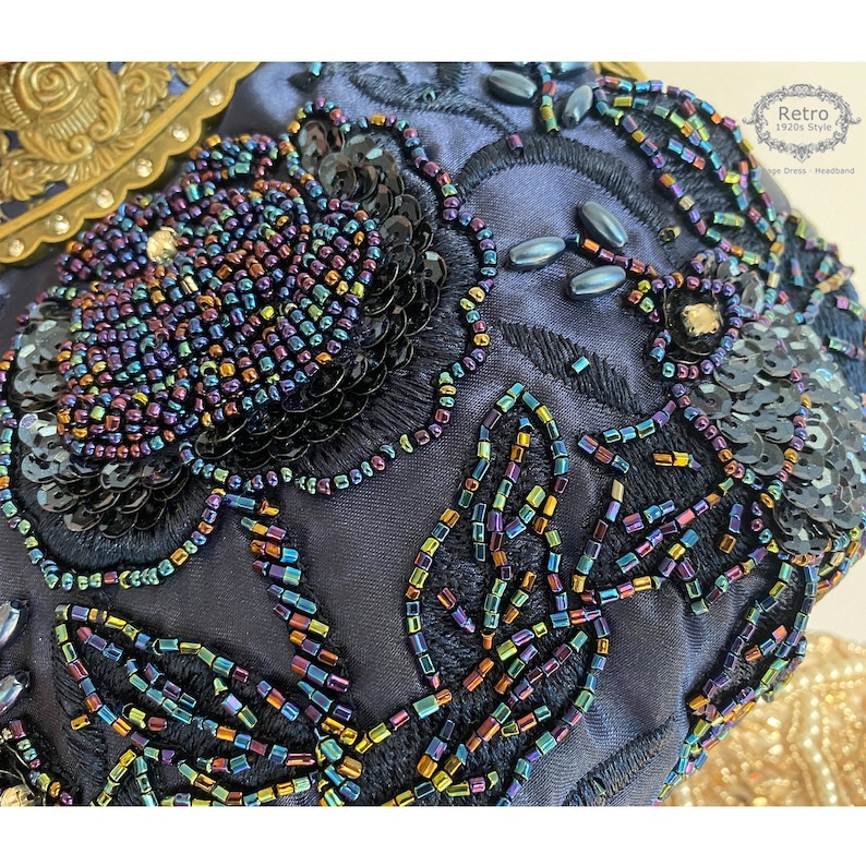 Pu&ograve; includere: Primo piano di un tessuto blu scuro con paillettes e perline iridescenti che formano un motivo floreale. Le paillettes e le perline sono disposte a forma di foglie e fiori.