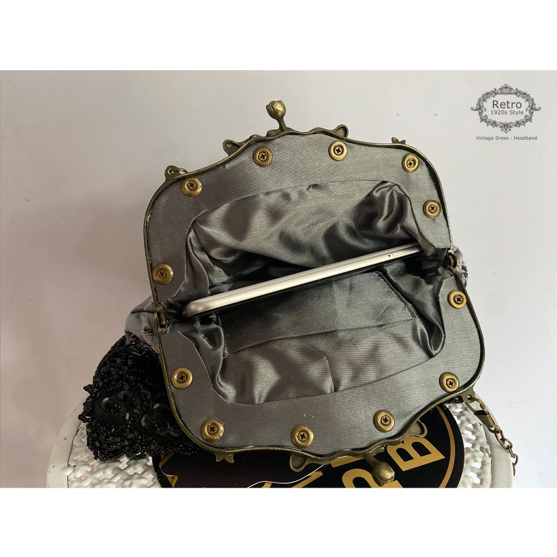 Pu&ograve; includere: Una pochette in stile vintage con un ricamo di perline e una cornice in metallo con dettagli decorativi. La pochette &egrave; aperta e l'interno &egrave; foderato con un tessuto grigio.