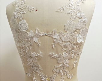 May include: White floral lace applique with pearl embellishments. The lace is delicate and intricate, with a variety of flower shapes and sizes. The applique is perfect for adding a touch of elegance to any garment.