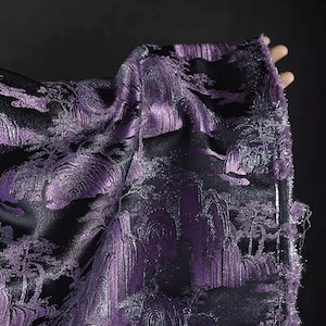 Könnte beinhalten: Nahaufnahme eines Stoffstücks mit Landschaftsdesign. Der Stoff ist tiefviolett mit schwarzem Hintergrund. Die Landschaft zeigt Berge und Bäume.