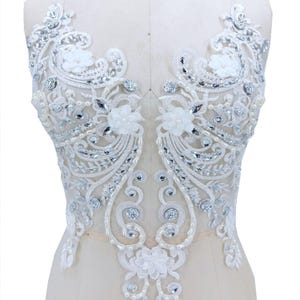 May include: White lace applique with floral and scroll designs, embellished with clear rhinestones and pearls. The applique features three-dimensional fabric flowers, suitable for bridal or formal wear.
