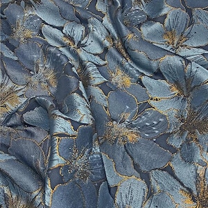 May include: Close-up of a fabric with a floral pattern. The fabric is a deep teal color with gold accents outlining the flowers. The flowers are large and stylized, creating a luxurious and elegant look. The fabric has a slight sheen, adding to its visual appeal.