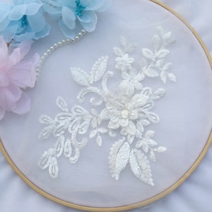 May include: White floral applique with sequins and a pearl bead center. The applique is on a white mesh background.