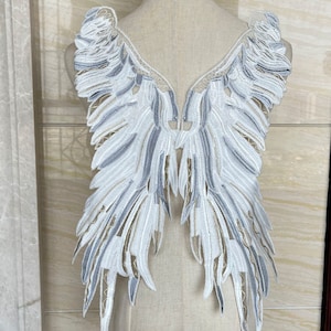 May include: White and gray lace angel wings with a delicate, intricate design. The wings are perfect for adding a touch of elegance to any craft project.