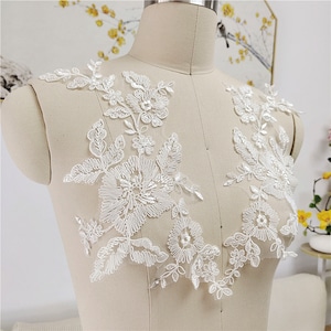 Puede incluir: Aplicación de encaje floral blanco con detalles intrincados. La aplicación presenta varios diseños de flores y hojas, perfecta para embellecer ropa de novia u otros proyectos de artesanía. El delicado encaje se muestra en un maniquí.