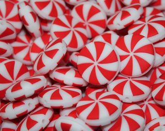 Puede incluir: Primer plano de un montón de cuentas de silicona de color rojo y blanco con forma de caramelo de menta. Las cuentas son lisas y tienen un patrón de espiral.