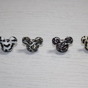 May include: Four small, round, plastic Mickey Mouse head-shaped buttons with different animal print designs. The buttons are black, white, brown, and pink with black spots.