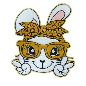 May include: A white bunny with a yellow and orange leopard print headband and yellow sunglasses. The bunny is smiling and giving the peace sign with both hands.