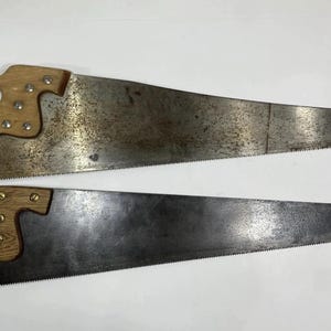 May include: Two hand saws with wooden handles and metal blades. The blades have a toothed edge for cutting. One saw blade has a darker, more aged appearance than the other.