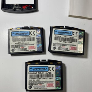 Puede incluir: Tres bater&iacute;as de iones de litio Motorola de 3,6V en color negro con etiquetas blancas que muestran especificaciones t&eacute;cnicas, textos de advertencia y pegatinas de seguridad hologr&aacute;ficas. Una bater&iacute;a est&aacute; marcada como Slim Main y otra como Standard Extra Capacity Main.