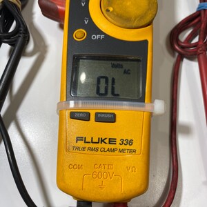 Pu&ograve; includere: Una pinza amperometrica Fluke 336 True RMS gialla con un display digitale che mostra OL e Volts AC. Il dispositivo presenta una grande manopola circolare, pulsanti funzione etichettati ZERO e INRUSH e puntali neri e rossi collegati alla base.