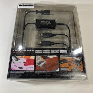 May include: A Roland UM-ONE mk2 USB MIDI interface in its original clear plastic packaging. The black interface unit features two MIDI connectors and a USB cable. The packaging includes text detailing compatibility, features, and usage examples.