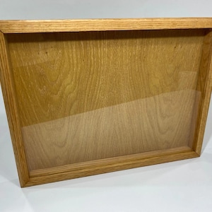 May include: A rectangular wooden display case with a clear glass front. The frame is made of light-coloured wood with visible grain. The case is empty, ready to showcase items.