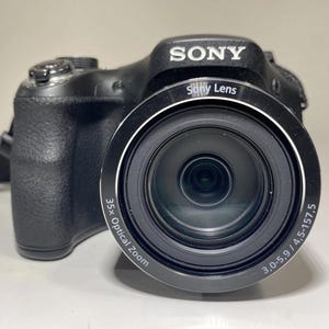 May include: Black Sony digital camera with a prominent lens. The lens has the text "Sony Lens" and "35x Optical Zoom". The camera body is black and has a textured grip. The lens specifications are 3.0-5.9/4.5-157.5.