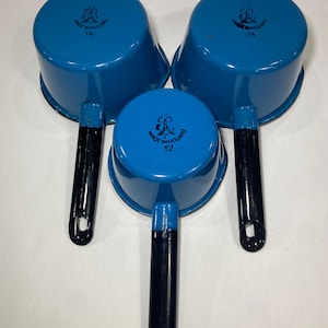 以下が含まれることがあります： 黒い取っ手が付いた青いエナメル製の鍋が3つ。鍋には「Made in England」と、12、14、16の数字が書かれています。