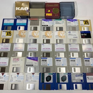 May include: A collection of thirty-six 3.5-inch floppy disks arranged in a grid, featuring various software labels including Adobe, Aldus FreeHand, and Norton Utilities, accompanied by two storage boxes labeled KAO and Dysan 100 with a 2 Disks Free sticker.