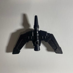 May include: Black plastic toy spaceship with a pointed nose and two wings. The spaceship has a detailed design with lines and grooves.