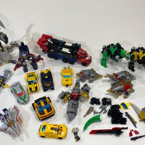 May include: A collection of various plastic robot action figures, including several vehicle-to-robot transformers, animal-shaped figures, and assorted small accessories like swords and blasters in red, yellow, blue, green, black, and grey colours.