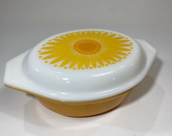 May include: A white oval casserole dish with a yellow sunflower design on the lid. The dish is made of glass and has a yellow base.
