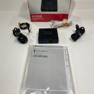 Könnte beinhalten: Pioneer CD-IB100II Interface-Adapter-Kit für iPod, bestehend aus einem schwarzen Adapter, Kabeln und einer Bedienungsanleitung. Das Set ist in einer weiß-roten Box mit dem Pioneer-Logo verpackt.