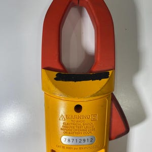 Pu&ograve; includere: Una pinza amperometrica gialla e rossa con un'etichetta di avvertenza che recita: WARNING TO AVOID ELECTRICAL SHOCK REMOVE TEST LEADS BEFORE OPENING CASE OR BATTERY DOOR. Il dispositivo include il numero di serie 78712912 e CAT III 600V per EN 61010.2.032.