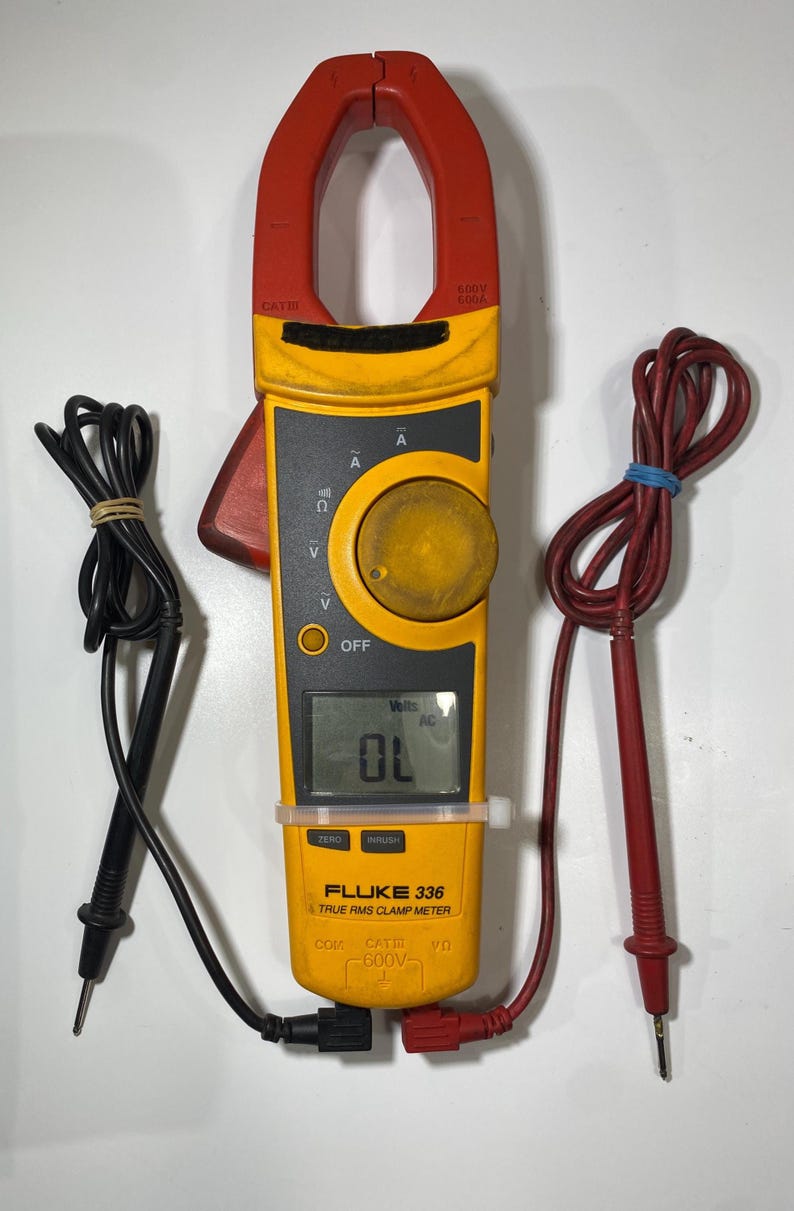 Pu&ograve; includere: Una pinza amperometrica Fluke 336 True RMS gialla e rossa con un display digitale che mostra OL. Il dispositivo &egrave; dotato di una manopola rotante, una ganascia rossa e due puntali collegati, uno con sonda nera e uno con sonda rossa.