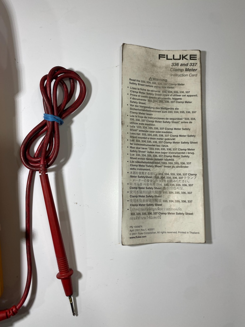 Pu&ograve; includere: Un puntale elettrico rosso con un elastico blu e una scheda di istruzioni bianca per la pinza amperometrica Fluke 336 e 337. La scheda presenta avvertenze multilingue, il logo Fluke, il numero di parte 1549876 e la data del 2001.