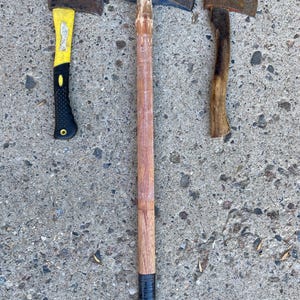 May include: Three tools are displayed: a hatchet with a yellow and black synthetic handle, a long-handled splitting maul with a blue metal head and a wooden handle, and a small hatchet with a weathered metal head and a curved wooden handle.