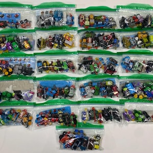 May include: A collection of twenty-one clear plastic storage bags, each filled with an assortment of small, multi-coloured toy trains and locomotive figures. The bags are arranged in a grid pattern, showcasing various designs, colours, and shapes.