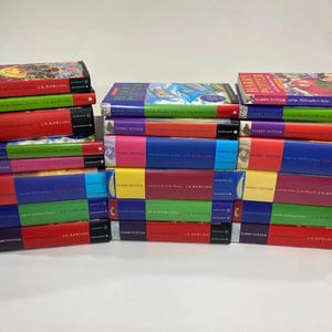 May include: A collection of Harry Potter books by J.K. Rowling arranged in three stacks. The books feature colourful spines and covers with various illustrations, including titles like The Philosopher's Stone, The Chamber of Secrets, and others.