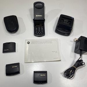 Puede incluir: Un tel&eacute;fono plegable Motorola Razr V3c negro, un folleto Motomanual, una base de carga negra, un adaptador de corriente negro con cable, dos fundas de tel&eacute;fono StarTAC negras y dos cubiertas de bater&iacute;a de tel&eacute;fono m&oacute;vil negras adicionales.