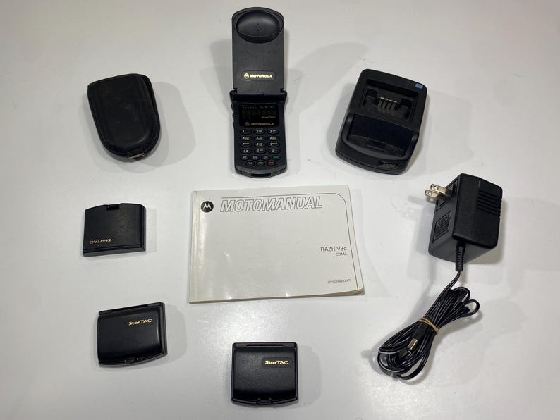 Puede incluir: Un tel&eacute;fono plegable Motorola Razr V3c negro, un folleto Motomanual, una base de carga negra, un adaptador de corriente negro con cable, dos fundas de tel&eacute;fono StarTAC negras y dos cubiertas de bater&iacute;a de tel&eacute;fono m&oacute;vil negras adicionales.